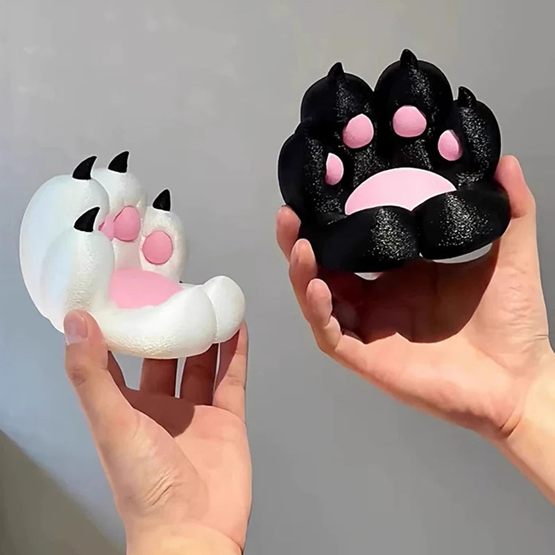 Two squishy cat paw toys in black and white, featuring textured pads, soft pink details, and small claws.