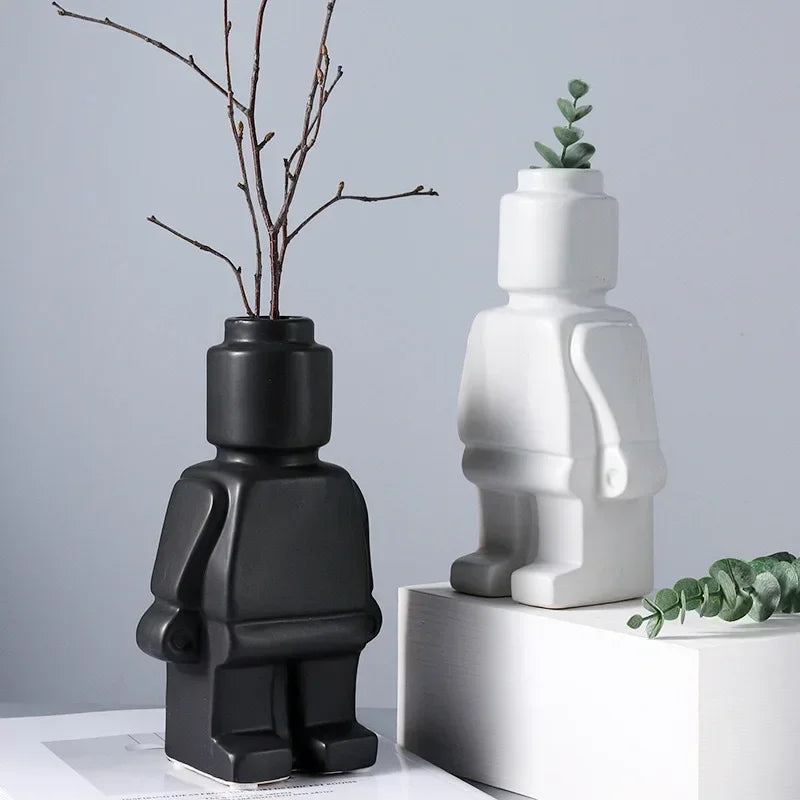 Two modern matte ceramic robot-shaped vases in black and white, standing on display with decorative stems.