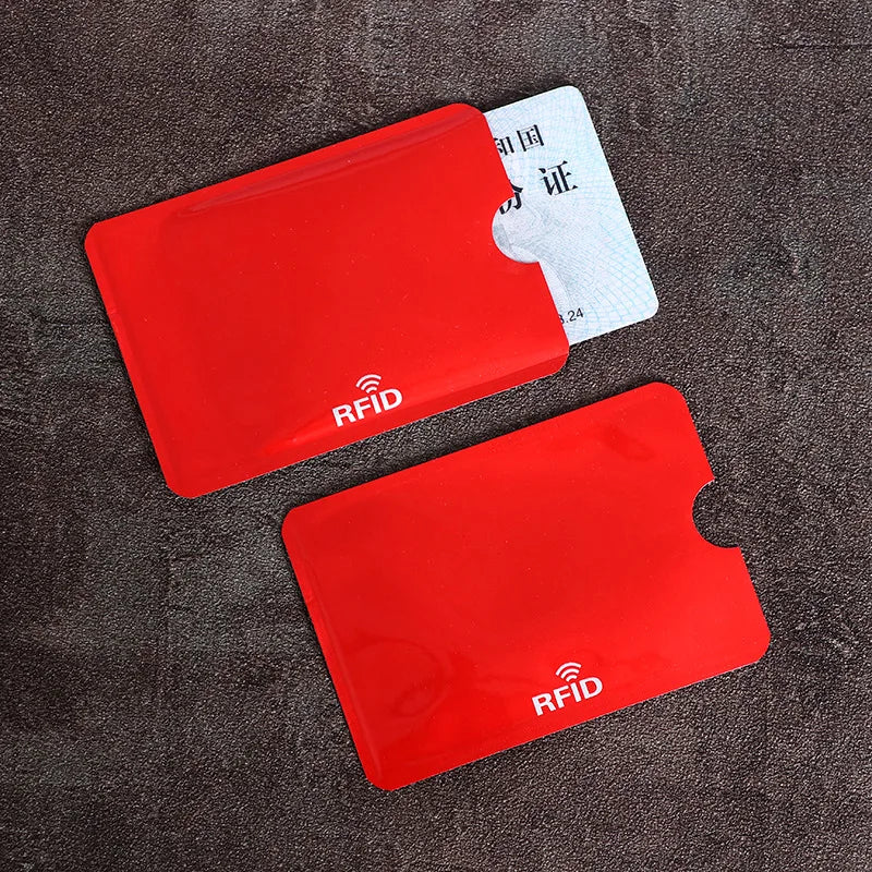 Two red plastic RFID-blocking card sleeves with thumb notches on a dark textured surface.
