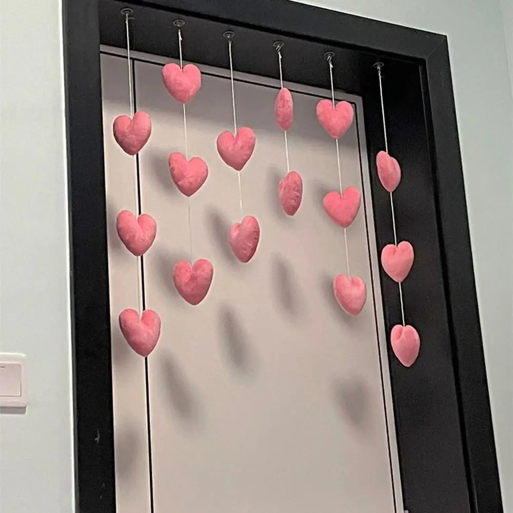 Decorative pink plush heart ornaments hanging on white strings, suspended in a doorway.