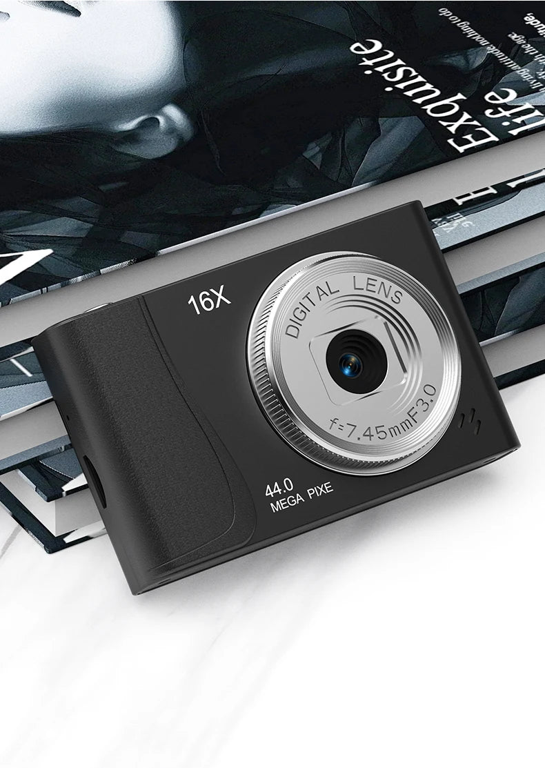Black digital camera with a silver lens, 16x zoom, and 44-megapixel sensor, resting on magazines.