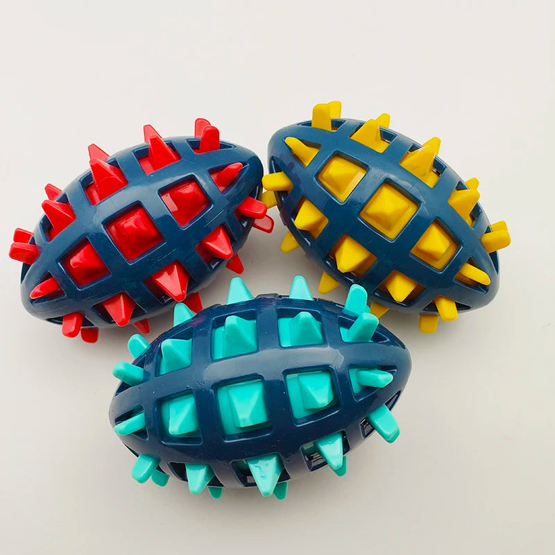 Three durable rubber rugby ball dog toys with dark blue cages and red, yellow, and turquoise spiked centres.