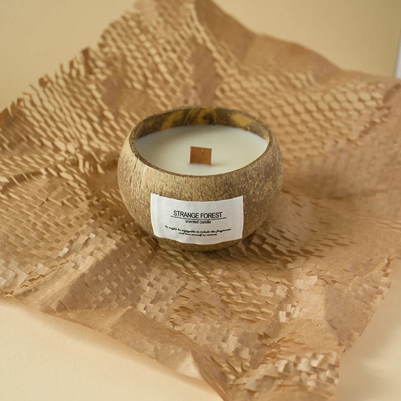 Scented candle in a natural coconut shell bowl with a wooden wick, set on rustic brown paper packaging.