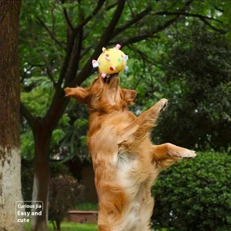 A golden dog jumping to catch a soft, yellow fleece ball patterned with colourful animal-shaped felt patches.
