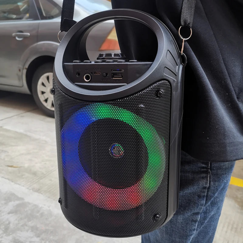 Black portable wireless speaker with a carry handle, shoulder strap, and a colourful LED light ring on the front.
