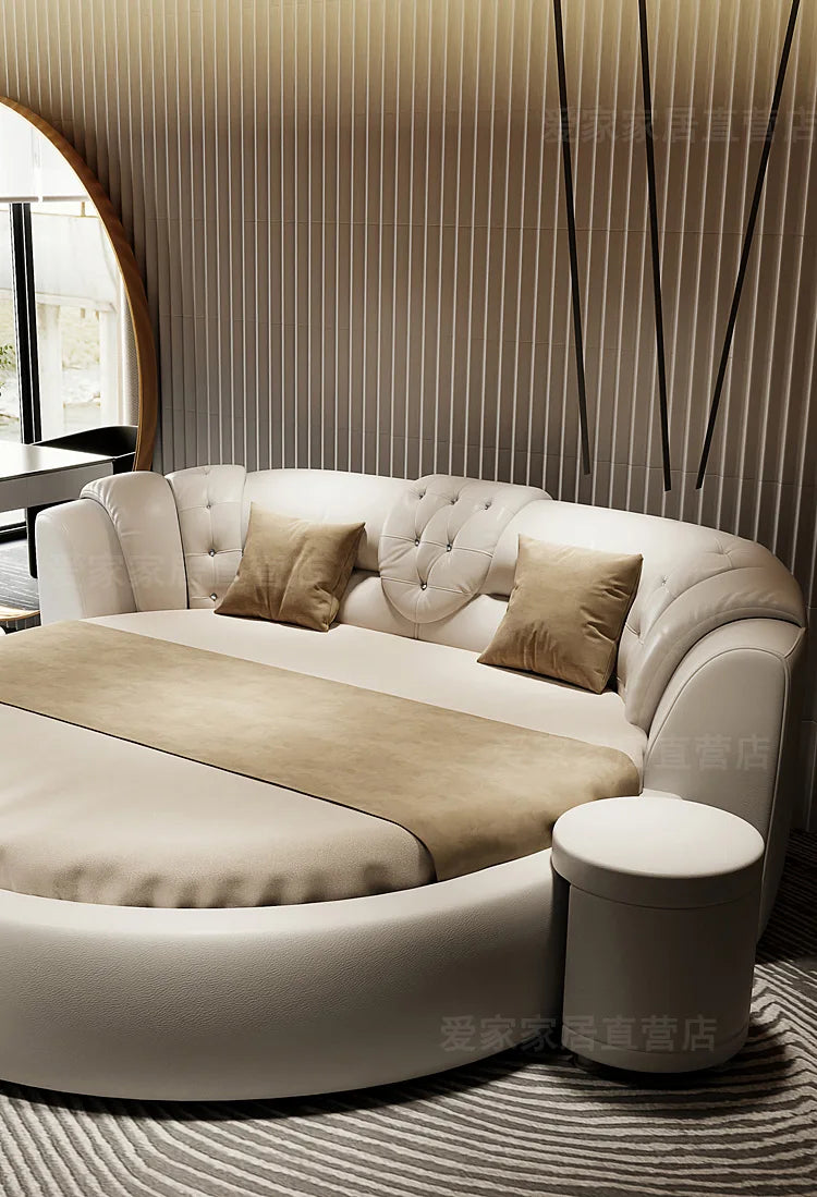 Modern round double bed in white faux leather with tufted detailing, beige cushions, and a matching circular stool.