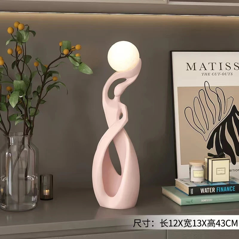 Abstract pale pink resin sculpture featuring a smooth, swirling silhouette topped with a glowing white spherical light.