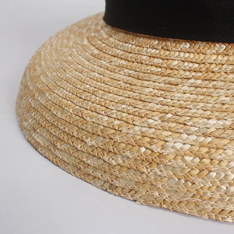 Close-up of a wide-brimmed straw sun hat in natural beige, featuring a classic woven texture and a black ribbon band.