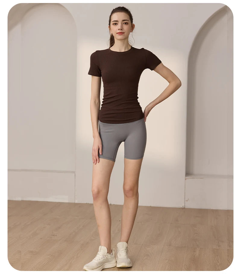 Model wearing a dark brown ribbed short-sleeve top and grey high-waisted gym shorts.