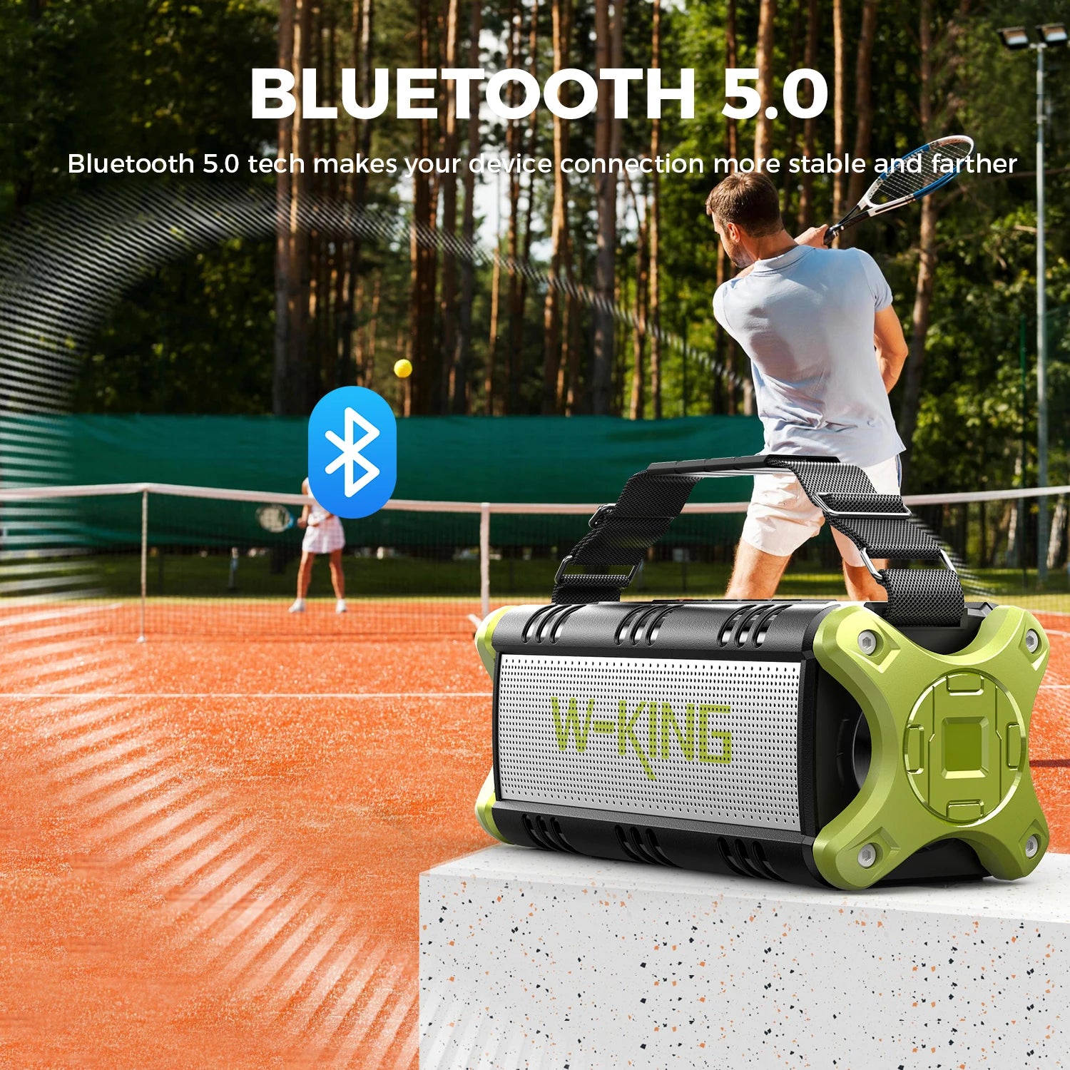 Black and olive-green portable wireless speaker with a carry strap, shown on a tennis court.