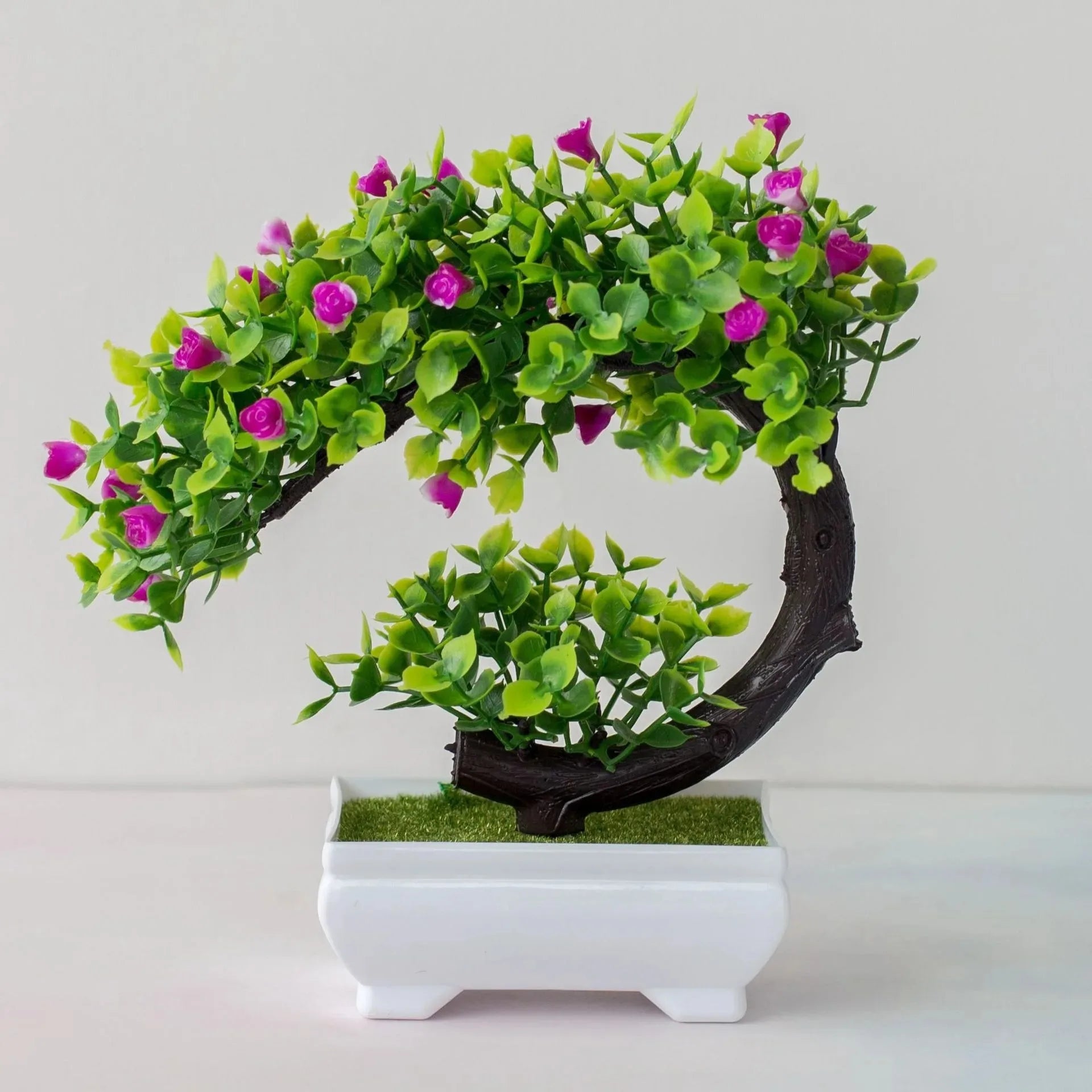 Artificial bonsai tree with vibrant green leaves and small pink flowers in a white rectangular ceramic pot.