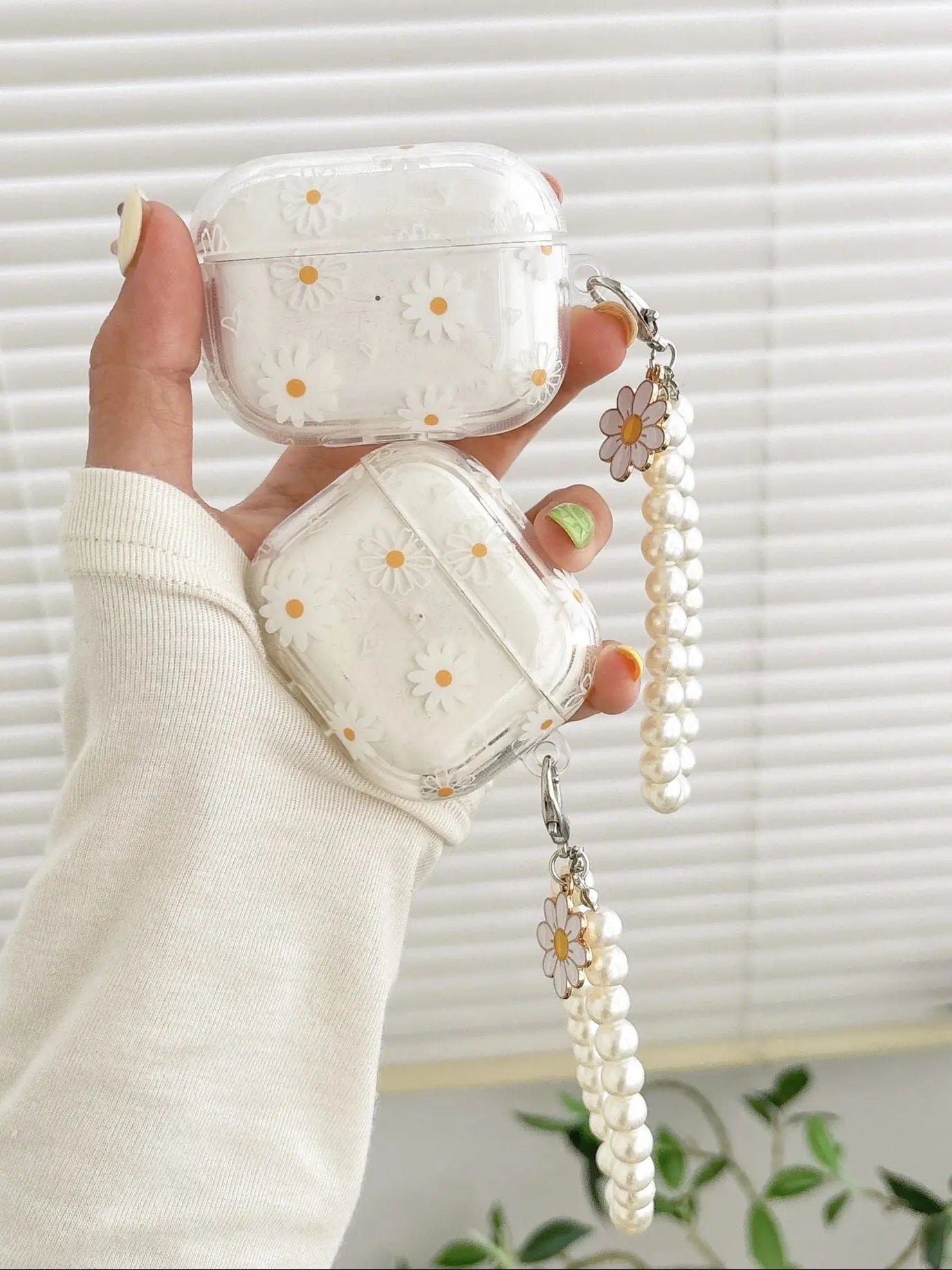 Clear daisy-print AirPod cases in TPU with matching pearl charm wrist straps. Compatible with AirPods Pro and Gen 1/2.