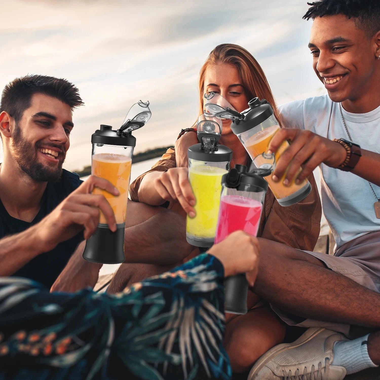 Three portable, clear and black electric blender bottles filled with colorful fruit smoothies held by friends.