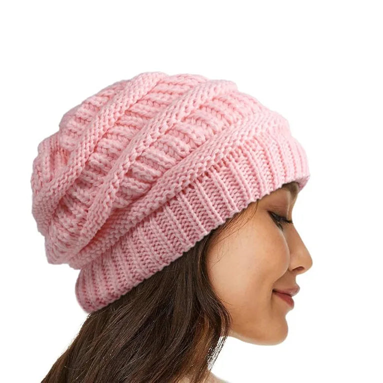 Side profile of a woman wearing a soft pink cable-knit beanie with a wide, ribbed cuff.