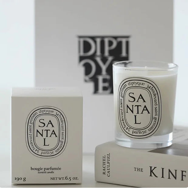 Santal scented candle in a clear glass jar with a matching white box, displayed on top of decorative books.