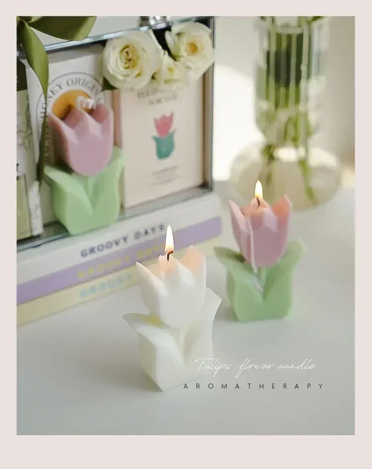 Two lit tulip-shaped candles in white and pink with green leaves, displayed on a table for an aromatherapy aesthetic.