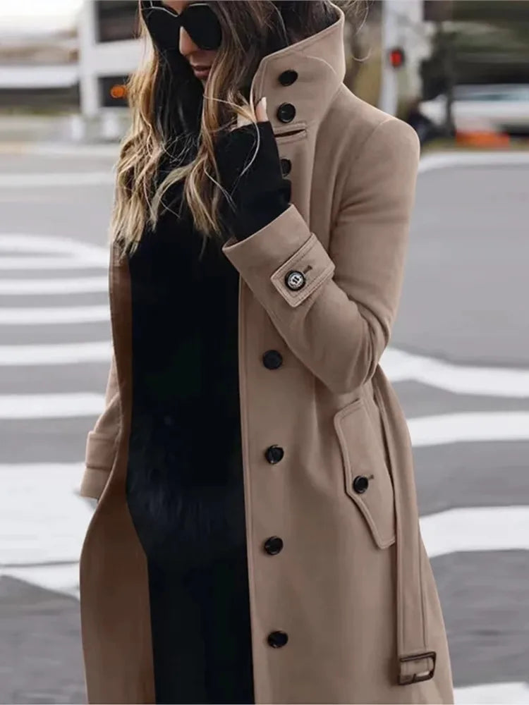 Woman wearing a beige, single-breasted wool trench coat with large black buttons, high collar, and belted cuffs.