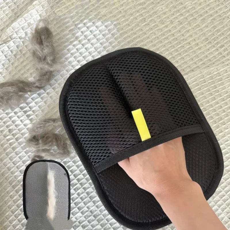 Black mesh pet hair removal mitt with a yellow tab, being used on a textured fabric surface to collect loose fur.