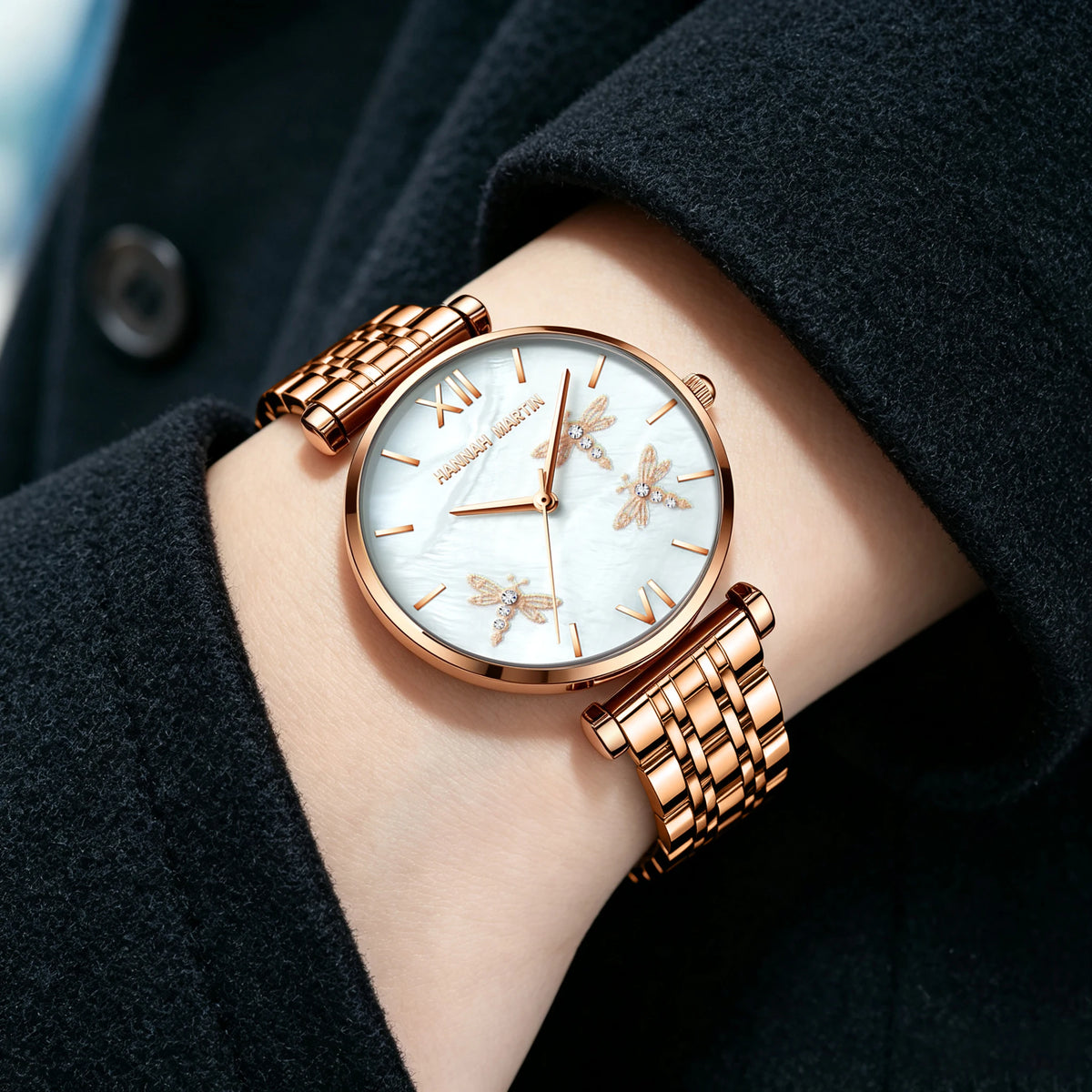 Hannah Martin rose gold quartz watch with round dial, dragonflies, and metallic link bracelet on a wrist.