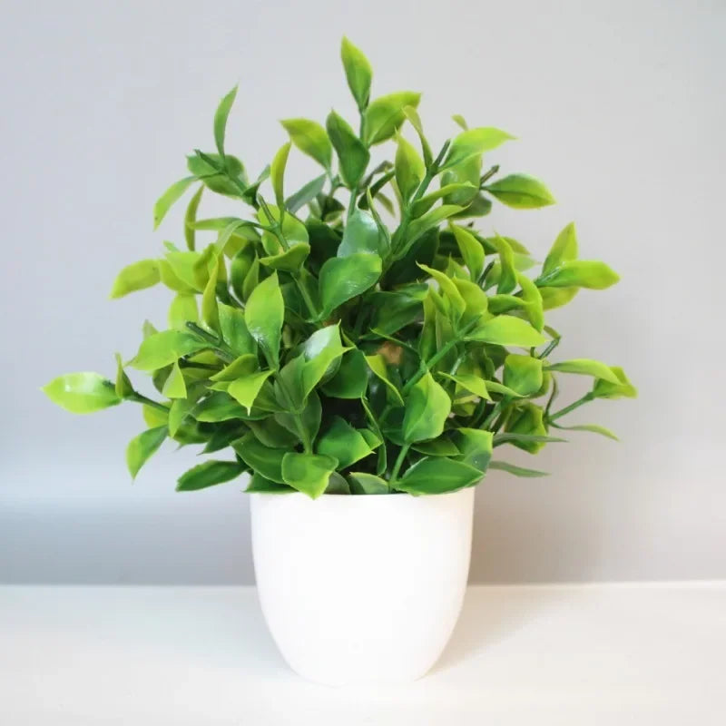 A small, bushy artificial green plant with glossy leaves in a simple white pot against a light gray background.