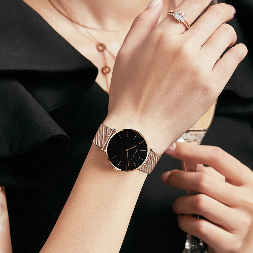 Rose gold minimalist women's watch with round black dial and mesh strap, worn on a wrist.