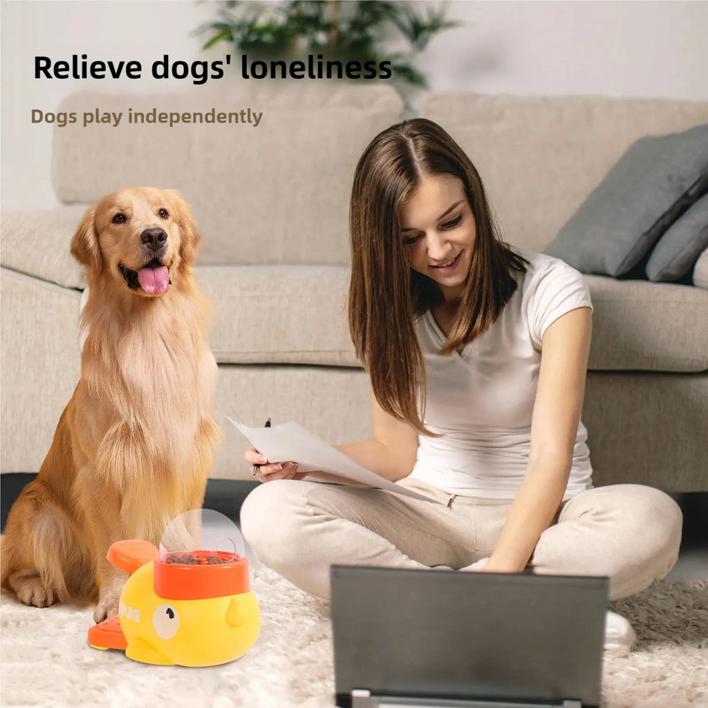 A golden dog sits next to a yellow, bird-shaped interactive treat-dispensing toy with a clear dome on the top.