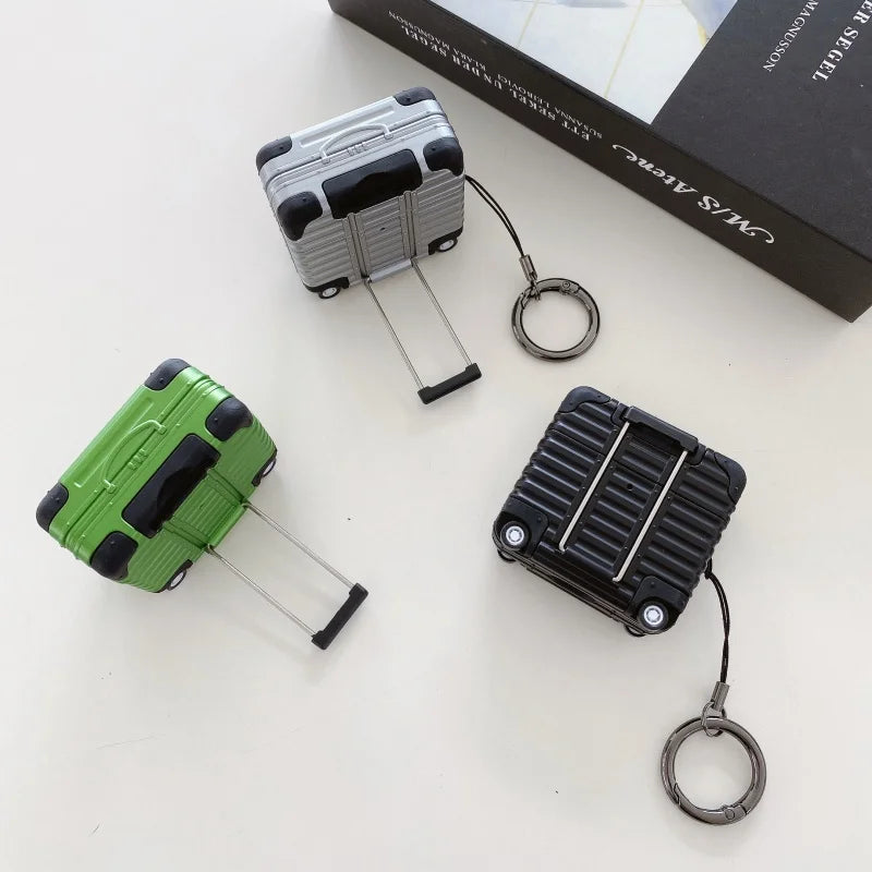 Silver, green, and black suitcase-style silicone cases for AirPods with integrated keyring and handle.