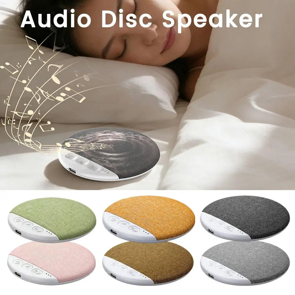 Round fabric-covered wireless sleep speaker, available in six colours, shown placed on a bed under a pillow.