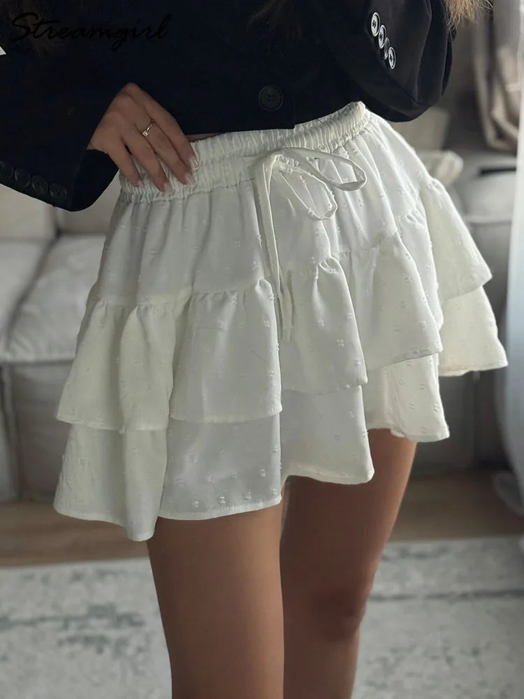 White tiered mini skort with a smocked elastic waistband, drawstring tie, and textured dotted fabric.