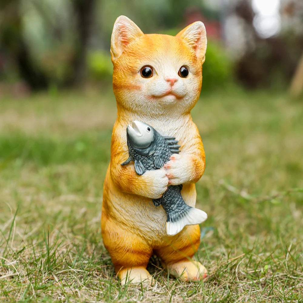Charming resin garden statue of a cute orange tabby cat standing on grass while holding a grey fish.