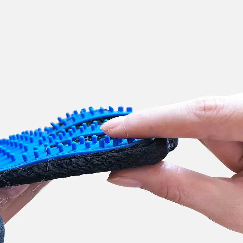 Close-up of a hand holding a blue silicone pet grooming glove with soft rubber massage nodules and a black fabric base.