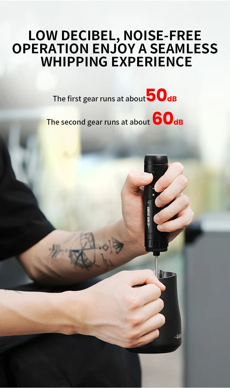 A person holding a sleek, matte black handheld electric milk frother, used for whipping liquids in a black pitcher.