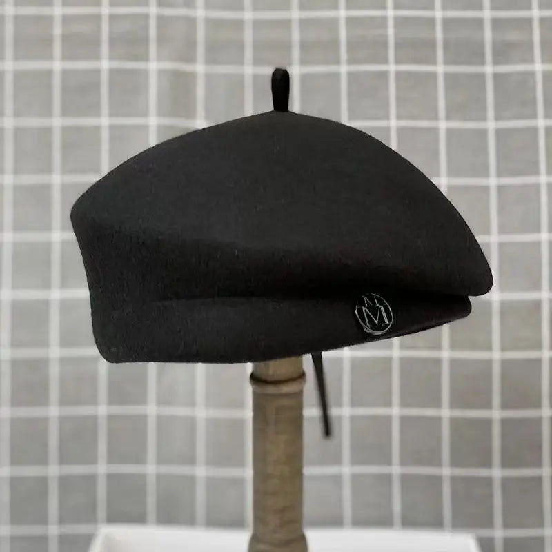 Classic black wool felt beret with a small centre stem and circular silver-tone accent on the side.