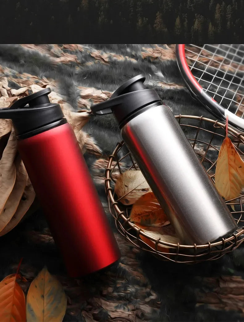 Two stainless steel sports water bottles in metallic red and silver, with black flip-top lids, on a textured surface.