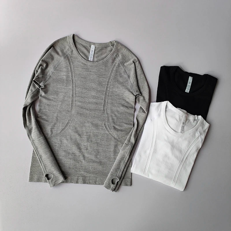 Three seamless, long-sleeved gym tops in grey, black, and white, featuring ribbed textures and thumbhole cuffs.