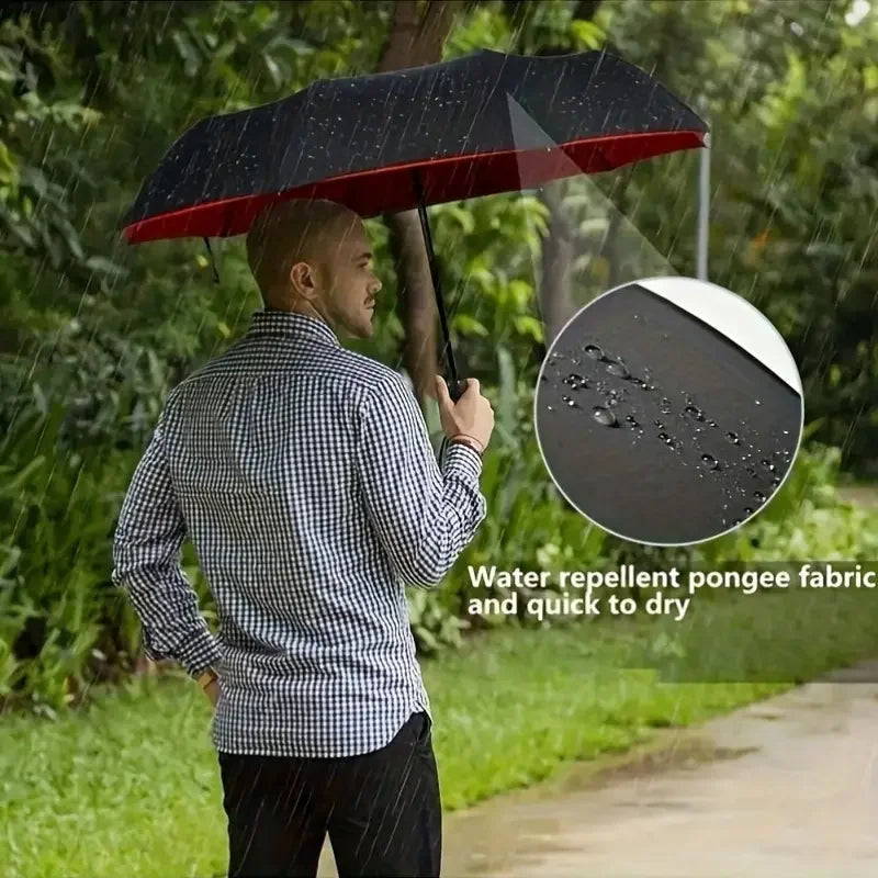 Man holding a large black and red folding umbrella in the rain with water droplets on the canopy.