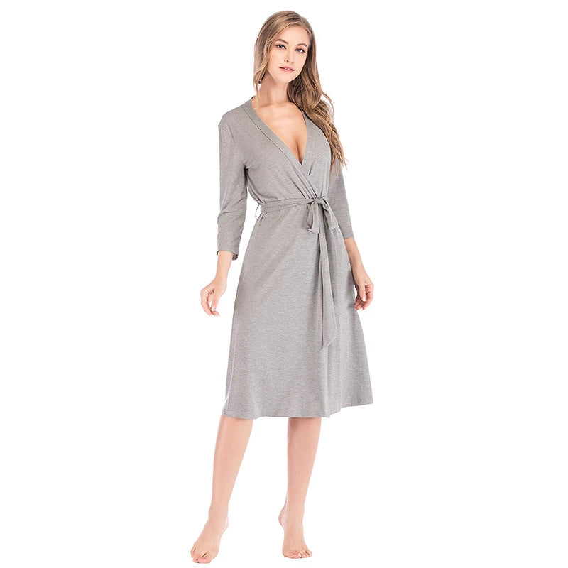 Woman wearing a soft grey midi-length wrap robe with three-quarter sleeves and a tie-waist belt.