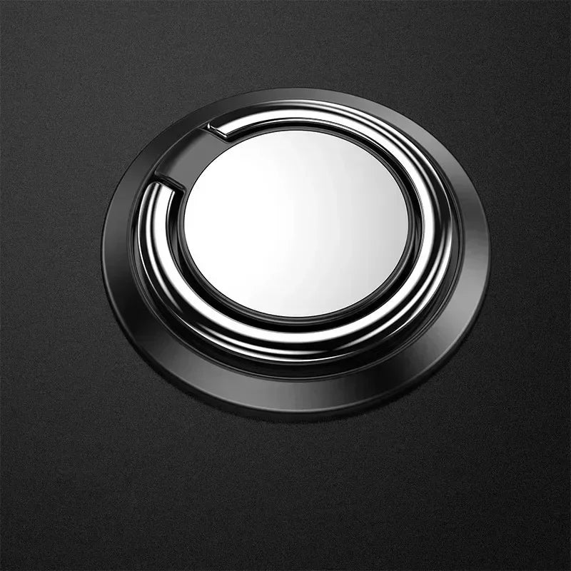 A sleek, round black and silver phone ring holder with a minimalist, polished metallic design on a dark background.