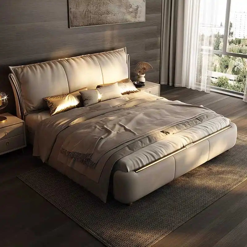 A modern double bed frame in soft beige with a large, padded headboard and sleek metallic gold accents.