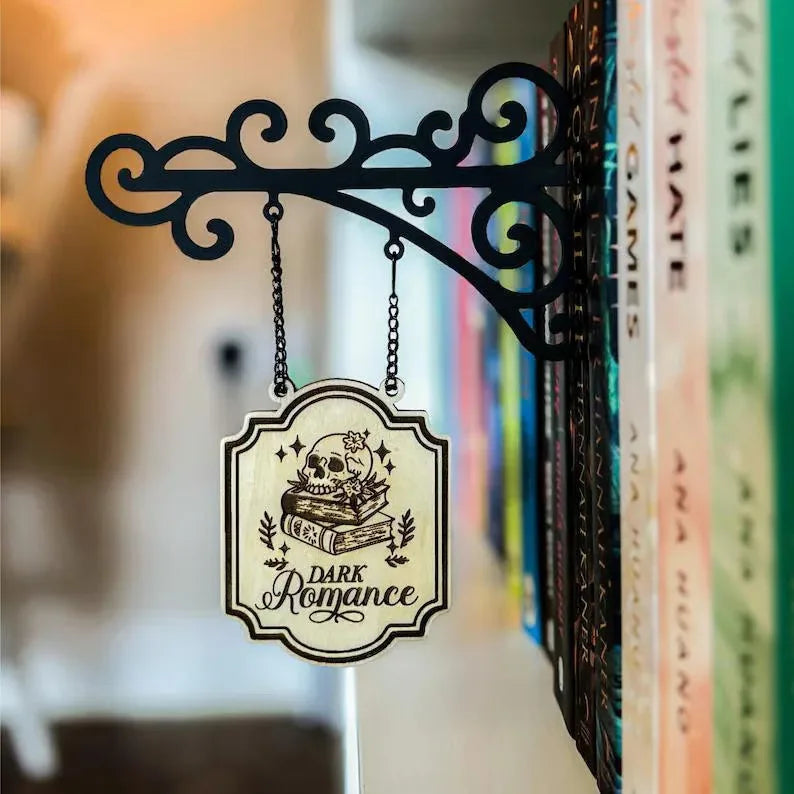 Decorative black scrollwork bracket hanging a cream-coloured sign featuring a skull, books, and 'Dark Romance' text.