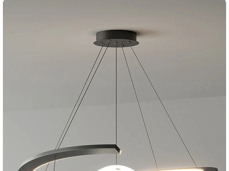 Modern black pendant ceiling light with a curved design and suspended glowing orb, featuring minimalist wire cables.