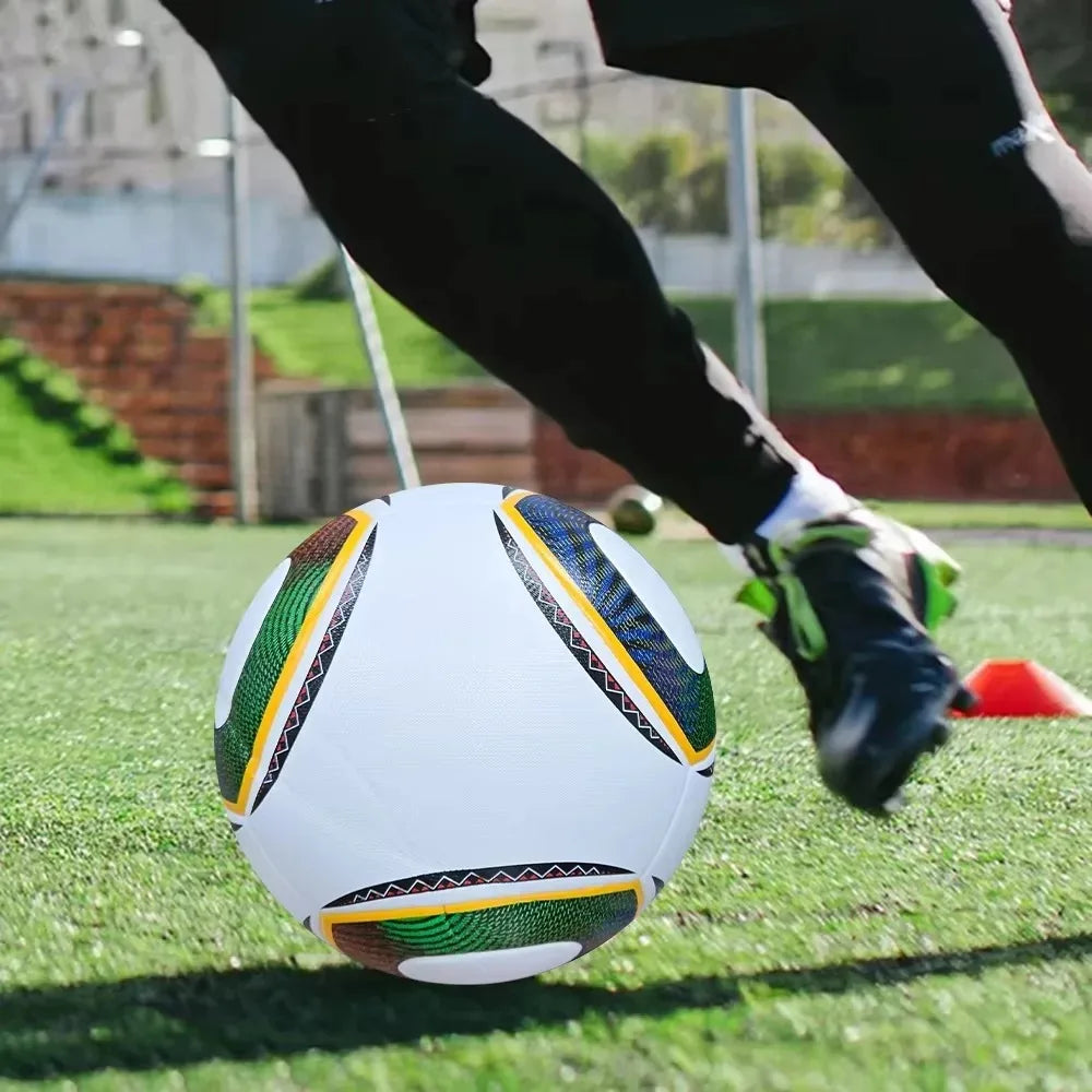 White football with textured green and blue patterned panels, being kicked on a grass pitch.
