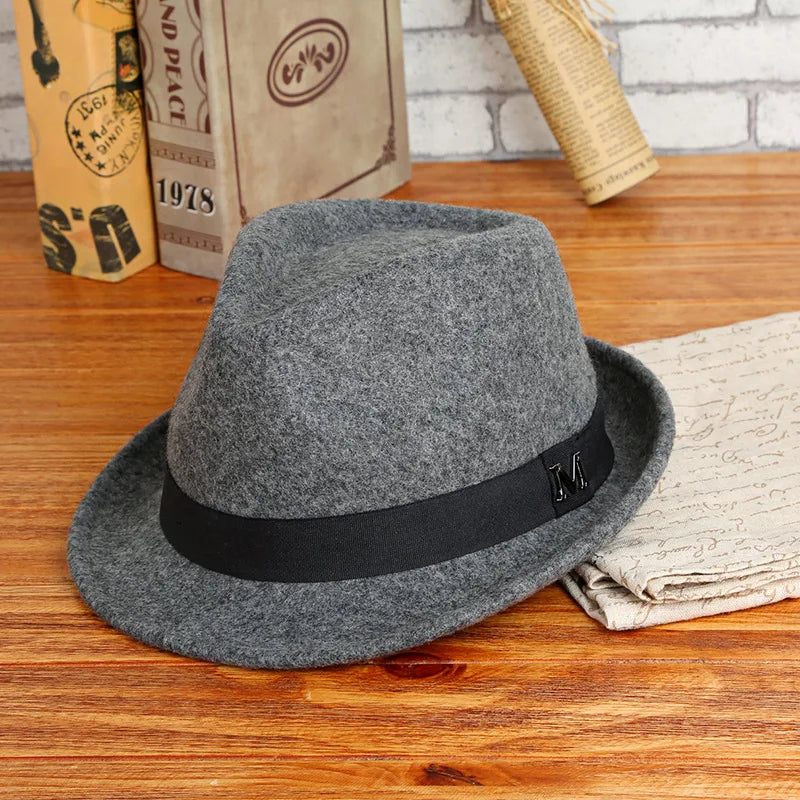 A classic grey wool felt fedora hat featuring a black ribbon band with a metallic 'M' detail.