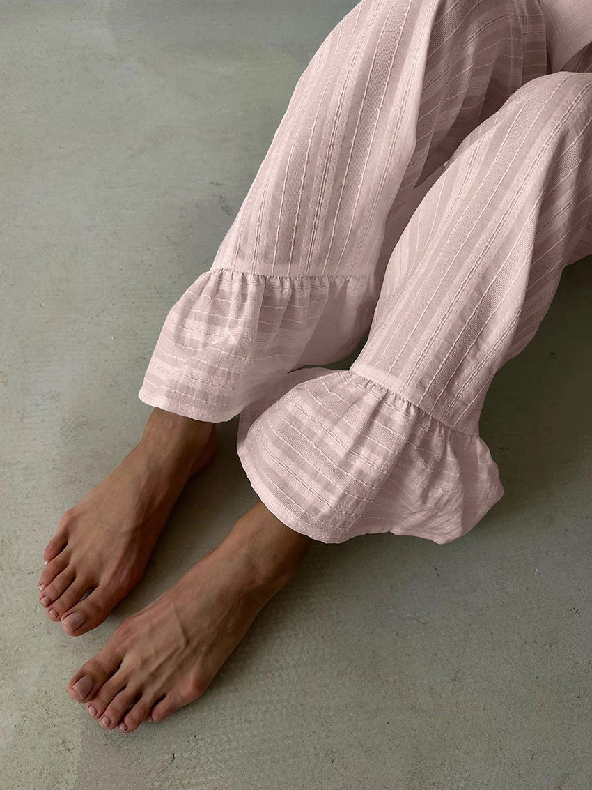 Soft pale pink lounge trousers in textured striped fabric featuring feminine ruffled hems.