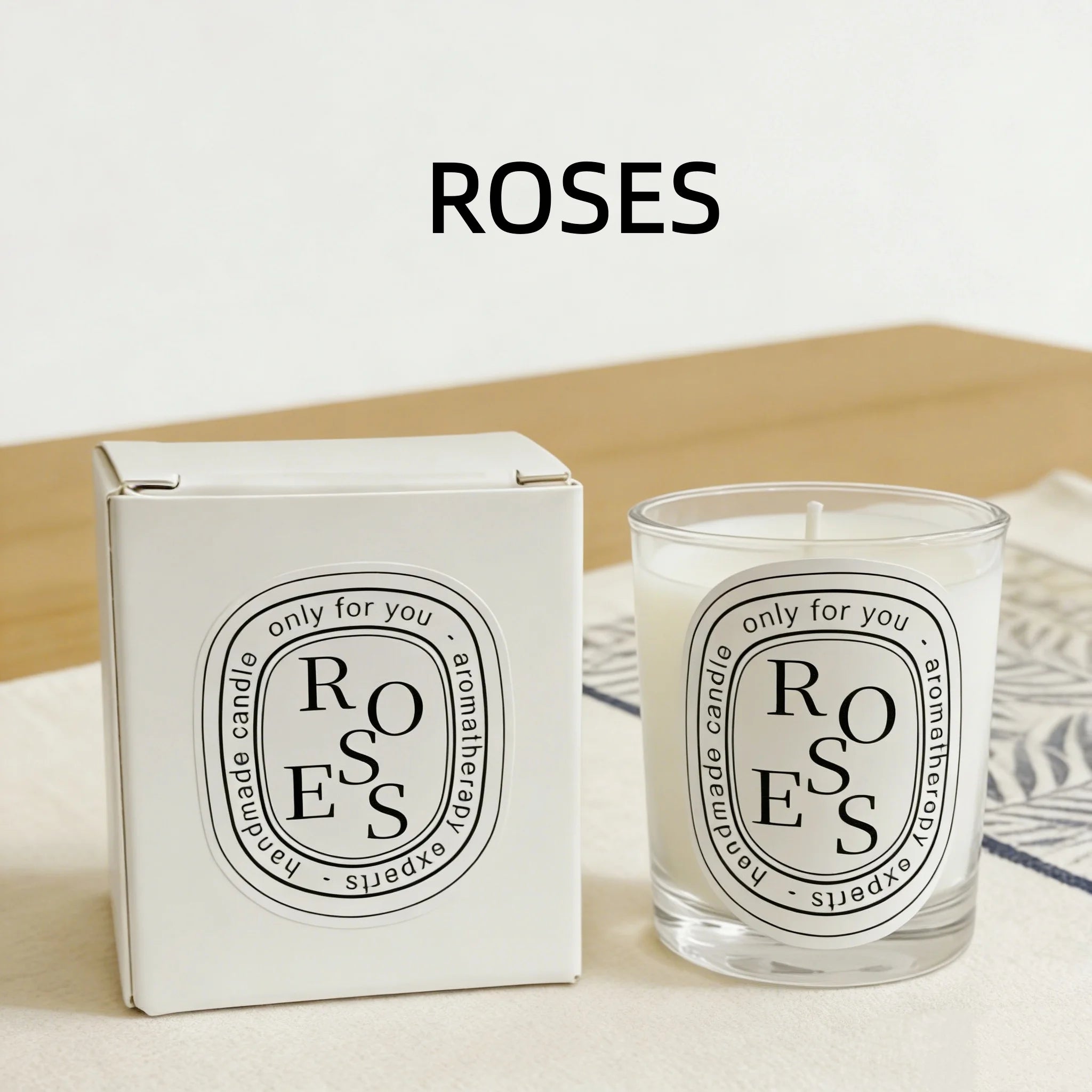 A white boxed scented candle and matching glass jar with a black and white oval "Roses" label.