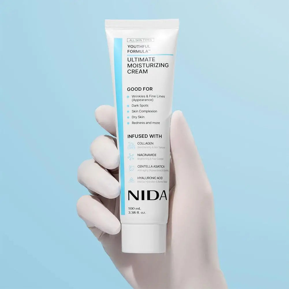 A white tube of moisturizing cream held in a gloved hand against a light blue background.