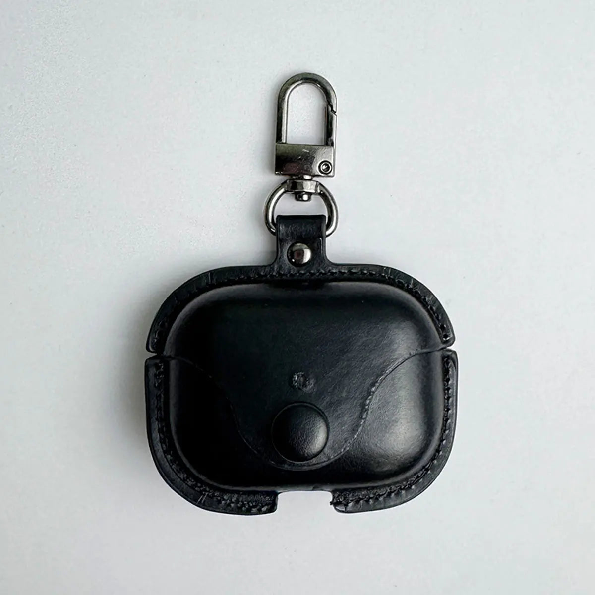 Black leather AirPods Pro case with a press-stud closure and silver keyring clip on a plain white background.