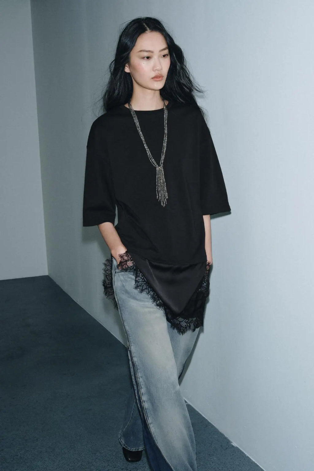Black short-sleeved t-shirt with a satin hem and delicate lace trim, paired with light-wash blue jeans.