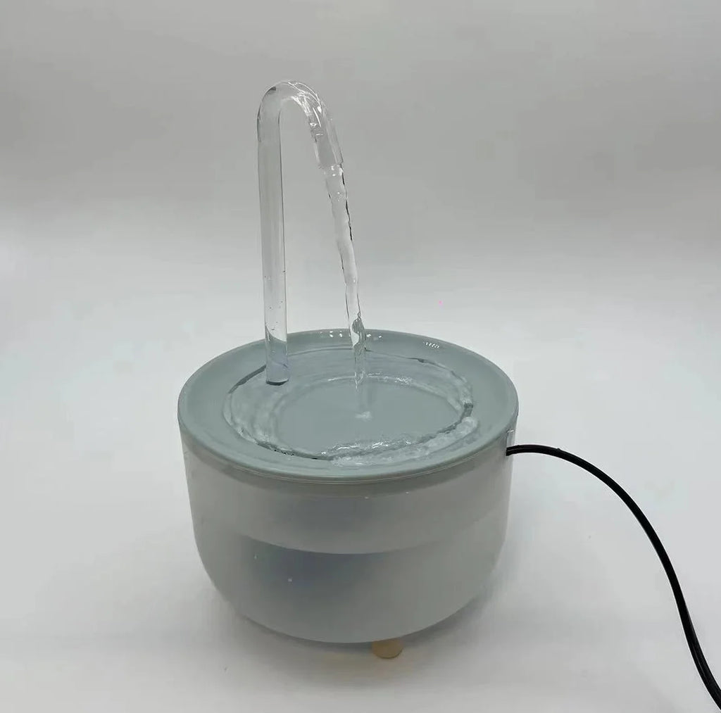 Light grey, modern pet water fountain with a clear arched spout, circular basin, and black power cord.