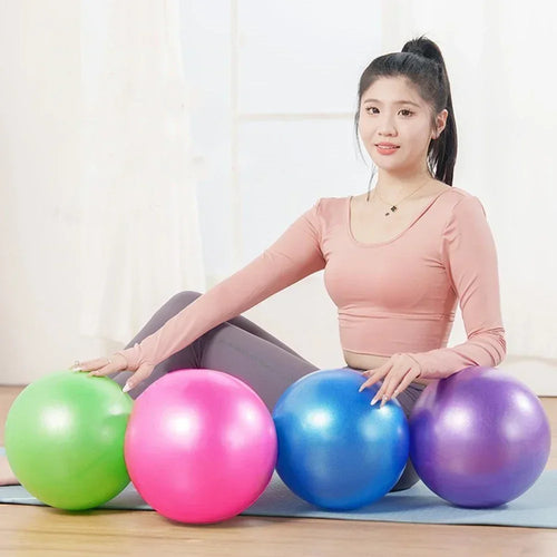 A woman in activewear sitting on a yoga mat with four colourful mini pilates exercise balls.